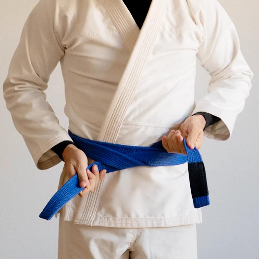 An athlete tying a blue belt over an unbleached gi